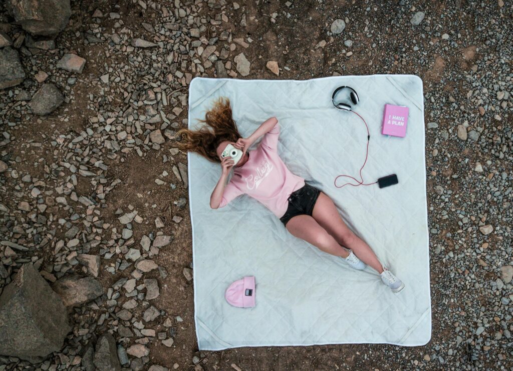 Aerial view of a woman relaxing outdoors with an Instax camera and headphones on a rocky terrain.